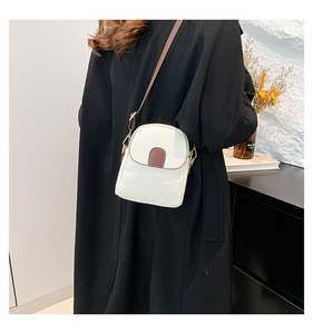 Detail view of a white crossbody bag with lychee texture and brown semi-circle decor