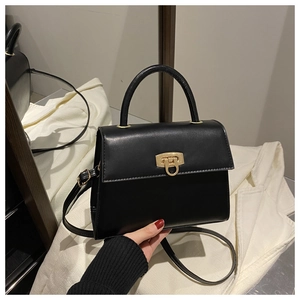 Detail einer schwarzen Handtasche mit goldenem Metallschloss und Tragegriff oben