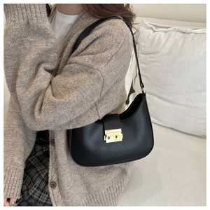 Detail of a black hobo shoulder bag with golden square buckle worn by a model in a soft room
