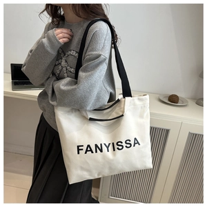 Side view of large canvas tote bag with black handles and FANYISSA print on cream fabric