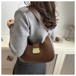 Detail of a brown matte leather underarm bag with gold metal buckle on a model