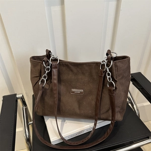 Large brown suede tote bag with chain strap displayed on a chair and art books