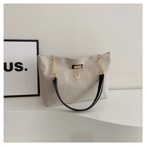 Detail of beige canvas tote bag with black leather straps and golden deer pendant