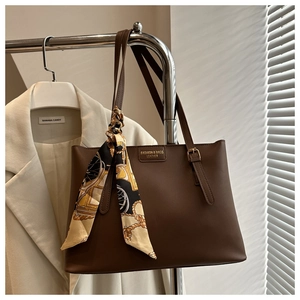 Detail of dark brown leather tote bag with elegant silk scarf and metal hardware