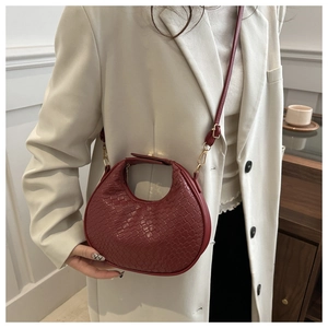 Detail of burgundy woven crescent bag with adjustable strap on cream blazer