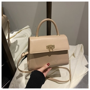 Detail einer eleganten beige Tasche mit goldenem Drehverschluss und praktischem Tragegriff