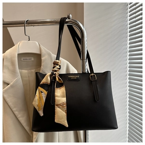 Detailed close-up of a black leather tote bag with elegant silk scarf and gold lettering