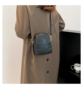 Detail of black leather crossbody bag with white stitching on a brown wool coat