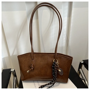Detail of a brown leather tote bag with decorative knots and tennis racket charm pendant