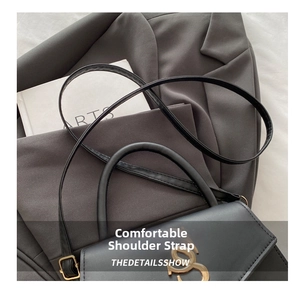 Detail of black leather handbag with gold metal logo and slender shoulder strap