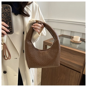 Detail shot of a brown crocodile texture hobo bag worn on the shoulder with a white coat
