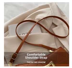Détail d'un sac bandoulière matelassé marron avec décoration en V doré sur un blazer
