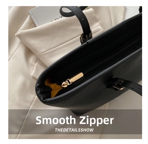 Detail of black Saffiano leather tote bag featuring gold zipper and yellow contrast lining