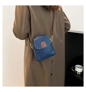 Vertical blue lychee grain leather crossbody bag shown on a brown trench coat