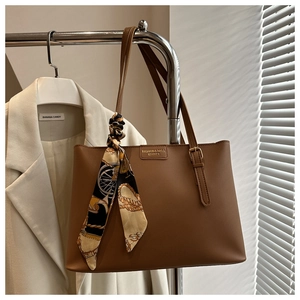 Detail of a brown leather tote bag featuring a metallic logo and a printed silk scarf