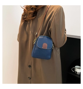 Crossbody small square bag in dark blue leather shown as worn by a model from a side view