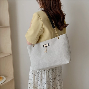 Large grey canvas tote bag with chain strap and deer pendant worn by a model