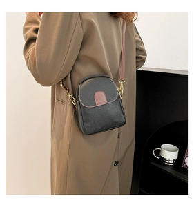 Detail of black pebbled leather crossbody bag with brown straps and gold metal hooks