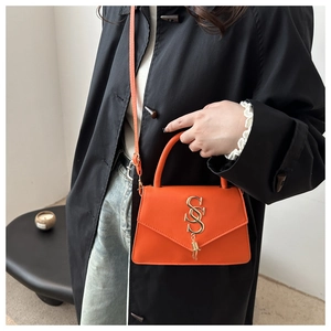 Detail of orange envelope crossbody bag showing the golden metal logo and smooth faux leather