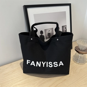 Black canvas tote bag with white FANYISSA lettering on a minimalist wooden table