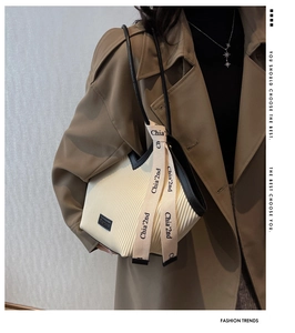 Detail of cream pleated tote bag with black trim carried by model in a trench coat
