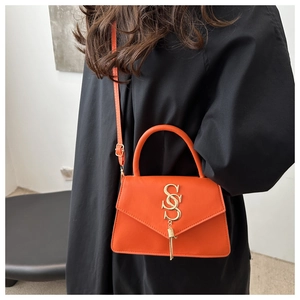 Detail of bright orange envelope bag with gold SSS metal logo and tassel on black coat