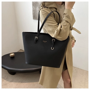Detailed view of black textured leather tote bag with gold logo on khaki trench coat