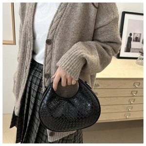 Detail of hand-woven black leather crescent handbag carried by a model in a cozy room