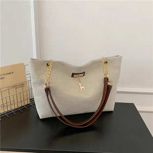 Beige canvas tote bag with brown leather gold chain strap and deer charm on black desk