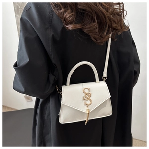 Close-up of a white leather bag with gold metal logo and tassel worn on a black shirt