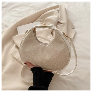 Detail of white crescent bag with crocodile pattern and golden zipper on beige background
