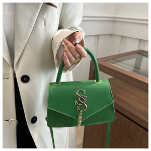 Detail of bright green leather handbag featuring golden S logo and elegant tassel charm