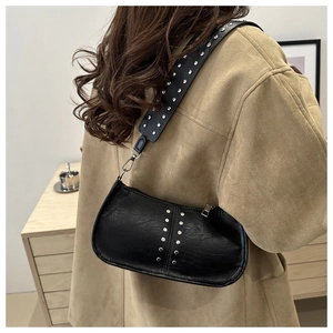 Détail du sac bandoulière vintage en PU noir à rivets porté avec un manteau beige
