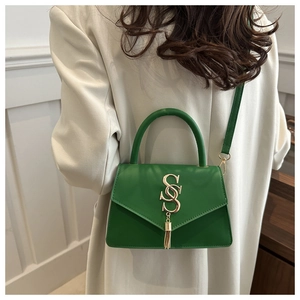 Detail of green leather handbag with gold SS logo, tassel accent and adjustable shoulder strap