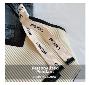 Close-up of white pleated tote bag featuring branded webbing strap and vertical texture