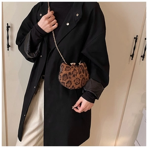 Detail of leopard print crossbody bag with gold cat-ear clasp worn over black coat