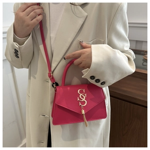 Detail of rose pink handbag featuring gold letter logo, tassel charm and leather strap