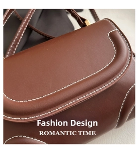 Detail of brown leather handbag featuring contrast white stitching and matte gold buckle