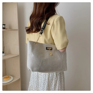Detail of a beige canvas tote bag with chain strap and gold deer pendant on a model