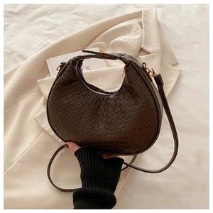 Close-up of dark brown crescent bag with woven texture on a white blazer background