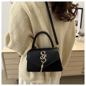 Detail of black leather handbag featuring golden SS logo and elegant tassel accents