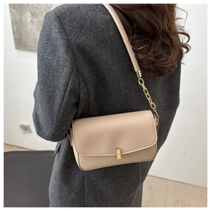 Detail of minimalist beige shoulder bag with gold clasp and chain strap on a grey coat