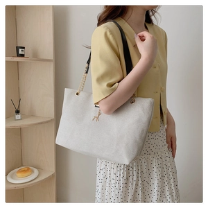 Detail of canvas tote bag featuring golden deer charm and metal chain link strap