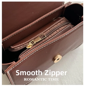Detail of smooth gold zipper and magnetic metal buckle on brown leather small square bag