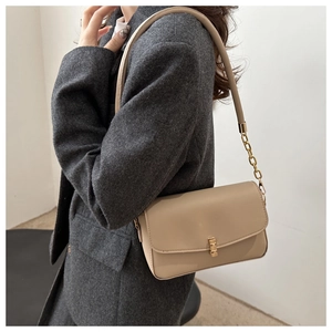 Detail of minimalist beige leather crossbody bag with gold metallic lock and chain strap