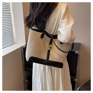 Détail du sac cabas en toile et cuir noir avec boucle dorée sur robe blanche