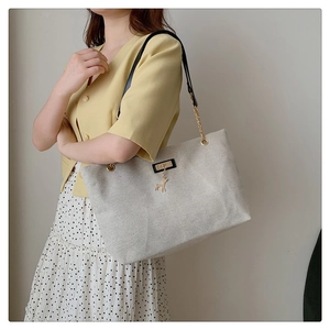 Detail of beige canvas tote bag featuring metal deer charm and gold chain leather strap