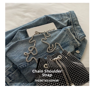 Detail der schwarzen Strass-Beuteltasche mit silbernem Kettenriemen auf Denim