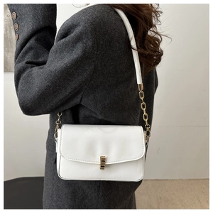 Detail of white leather shoulder bag with gold chain strap worn over a grey coat