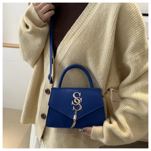 Detail of Klein blue handbag featuring a gold S-shaped logo and metallic tassel accents